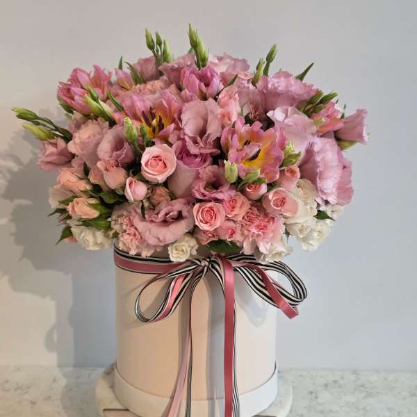 Pink floral arrangement in a round hat box with ribbon bow