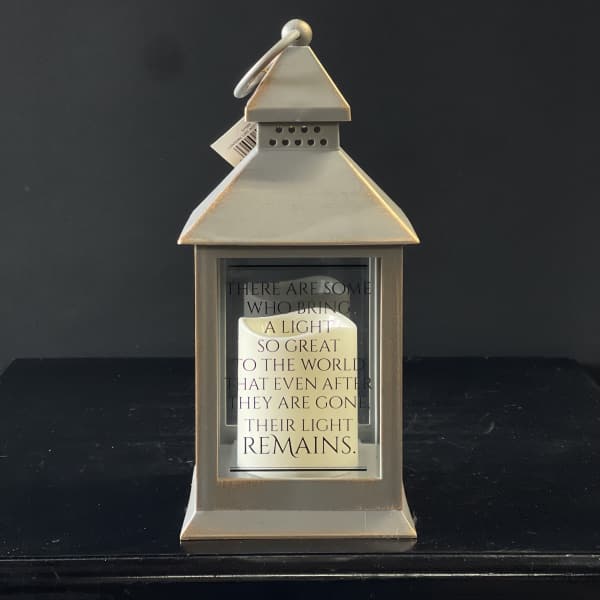 Beige metal lantern with glass sides, a memorial quote, and a white pillar candle inside.