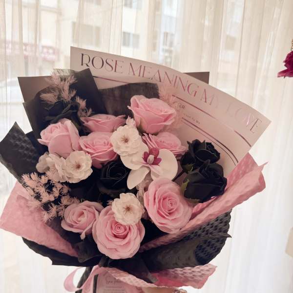 Pink and black rose bouquet with white accent flowers and decorative wrapping