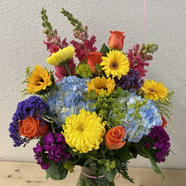 Colorful mixed bouquet in a glass vase with roses, hydrangeas, and daisies