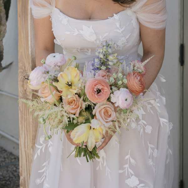 Bride holding a pastel bouquet of roses, ranunculus, and tulips