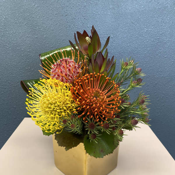Bright mixed bouquet in a gold square vase with yellow and orange blooms