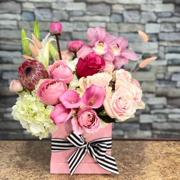 Pink floral arrangement in a pink box with a striped ribbon