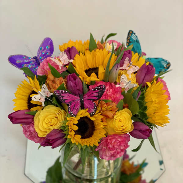 Bouquet of sunflowers, tulips, and roses in a glass vase with butterfly picks