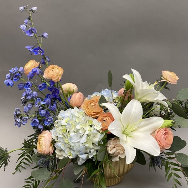 Mixed bouquet with white lilies, blue delphinium, and peach roses in a vase