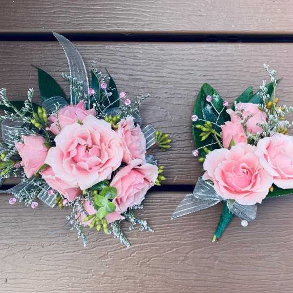 Two pink rose boutonnieres with silver ribbon and greenery