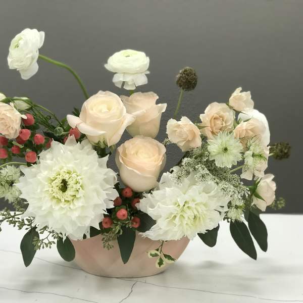 Blush roses and white blooms arranged in a low pink bowl