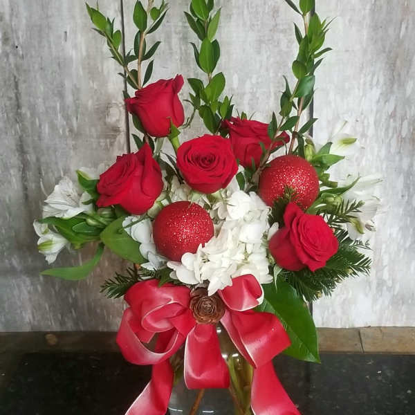 Red roses and white flowers in a glass vase with a red ribbon