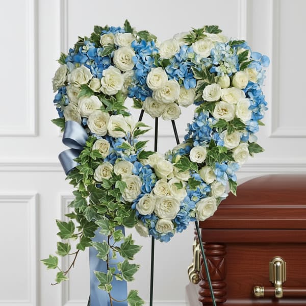 Heart-shaped floral wreath with white roses and blue hydrangeas on a stand