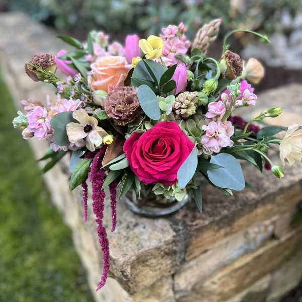 Mixed bouquet with a bright pink rose and pastel blooms in a glass vase
