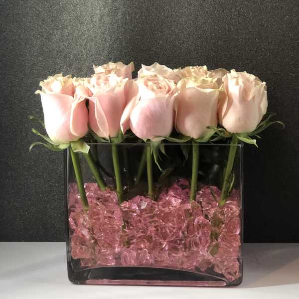 Pink roses arranged in a clear square vase with pink filler