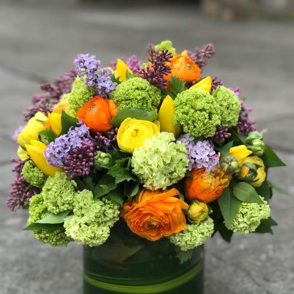 Bright mixed bouquet in a green glass vase with orange, yellow, purple, and green blooms