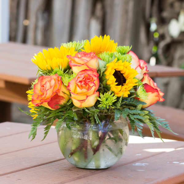 Bouquet of yellow sunflowers and peach-edged roses in a glass vase