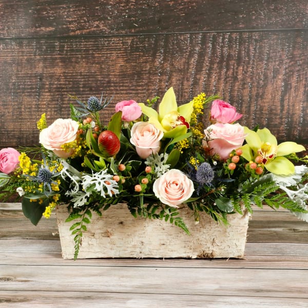 Low centerpiece of pink and peach roses with yellow orchids in a birch box