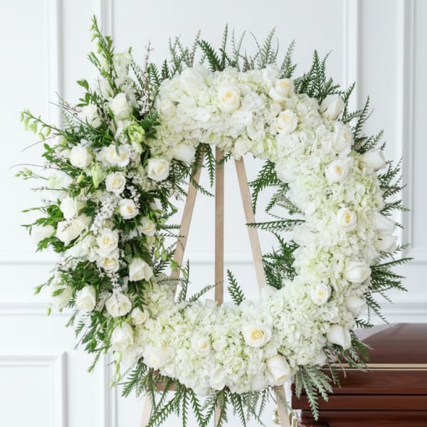 White floral funeral wreath on a wooden easel beside a casket