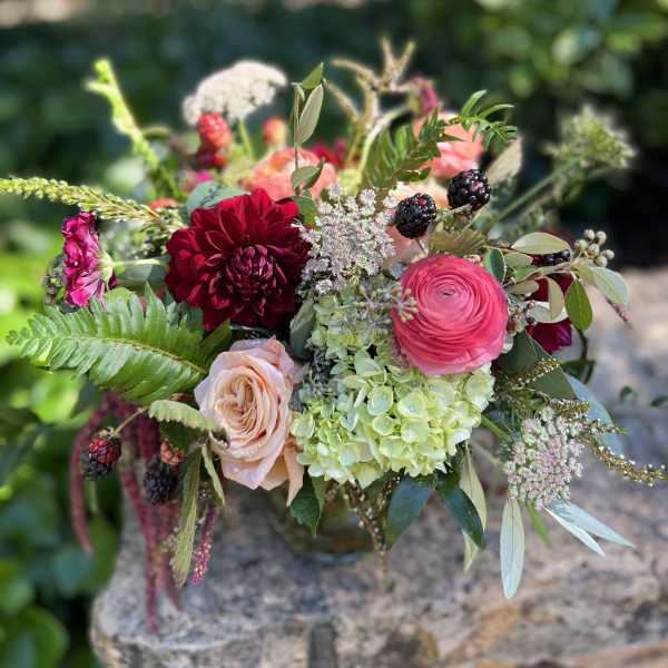Bouquet of red, pink, and peach flowers with berries in a vase