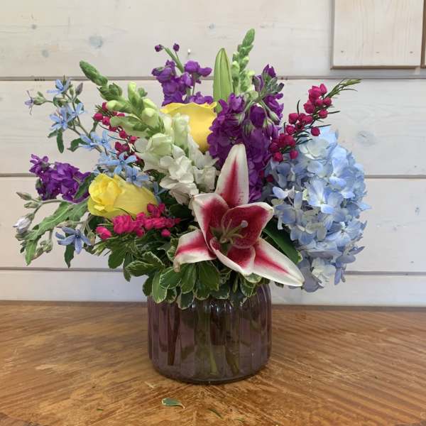 Mixed bouquet with lilies, roses, hydrangea, and purple blooms in a glass vase