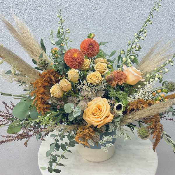 Orange roses and dahlias in a low vase with airy dried grasses