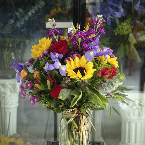 Mixed bouquet with sunflowers, roses, and purple iris in a glass vase