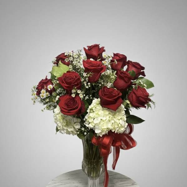 Red roses and white hydrangeas in a clear glass vase with a red ribbon