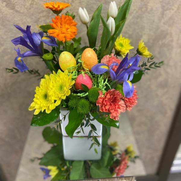 Colorful spring bouquet in a white square vase with decorative eggs