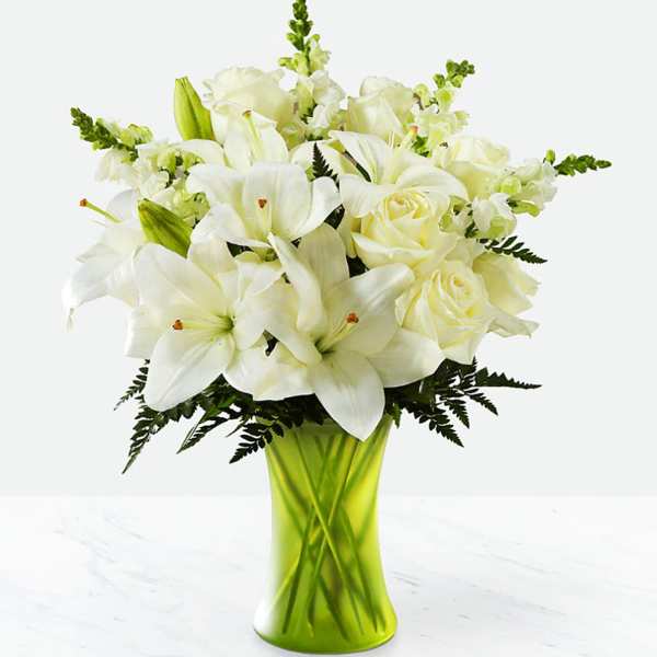 White lilies, roses, and snapdragons arranged in a bright green vase