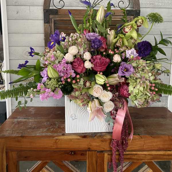 Large mixed floral arrangement in a white vase with pink ribbon