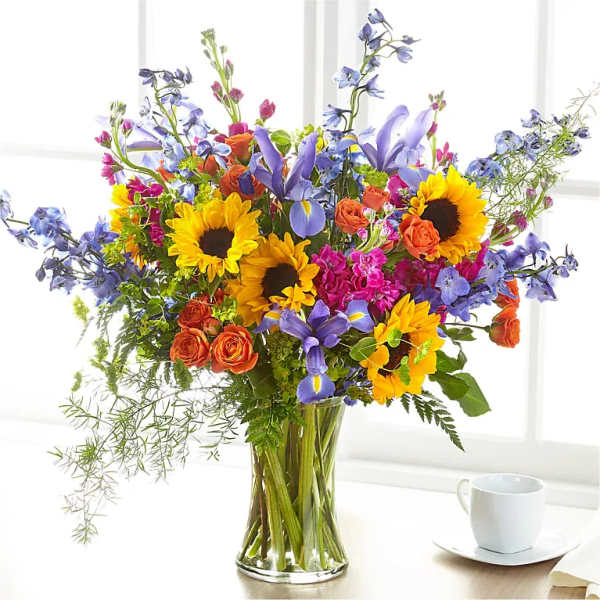 Mixed bouquet with sunflowers, purple irises, and orange roses in a glass vase