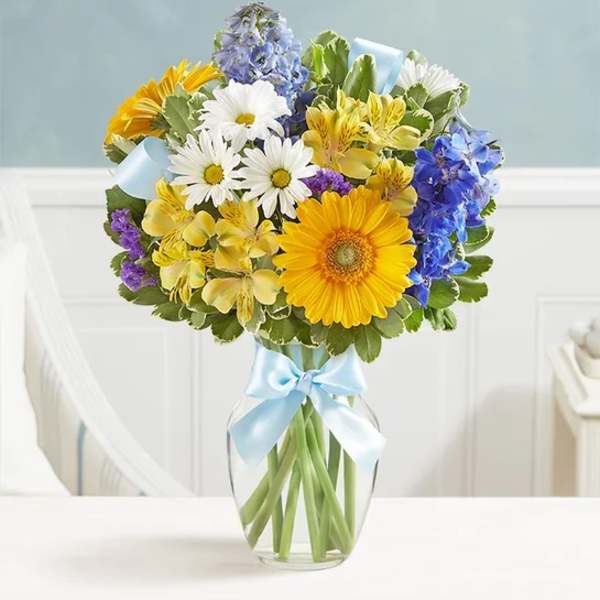 Mixed bouquet of daisies, gerberas, and blue flowers in a glass vase