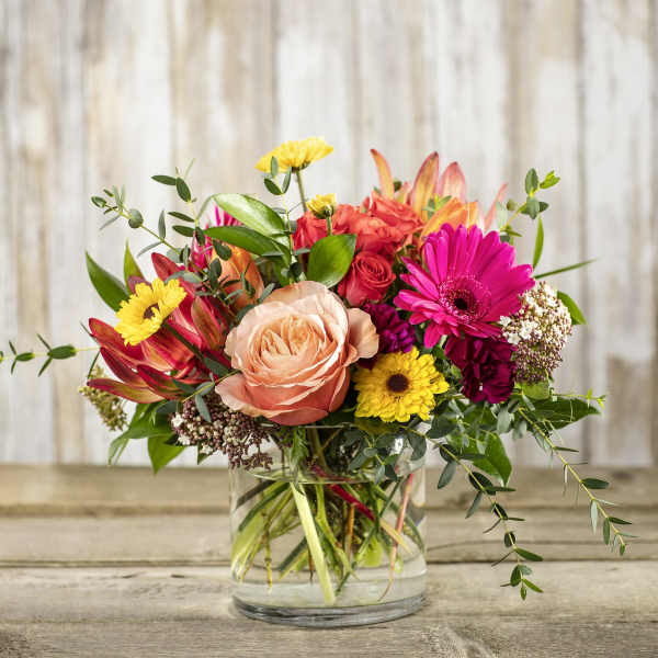 Mixed bouquet of roses, gerbera daisies, and other flowers in a glass vase