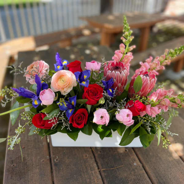 Mixed bouquet in a white rectangular vase with red, pink, purple, and peach flowers