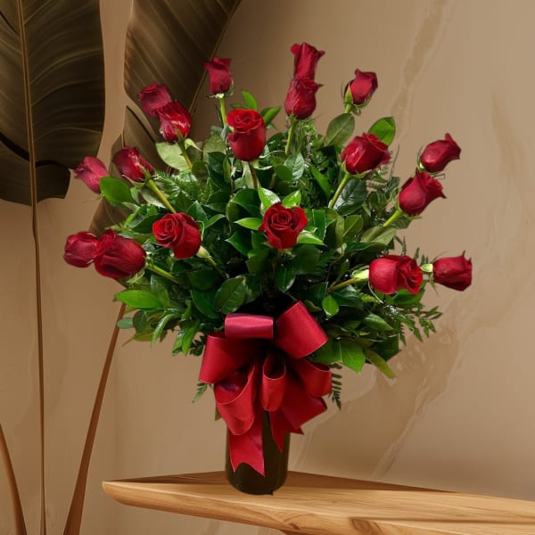 Red roses arranged in a black vase with a large red ribbon