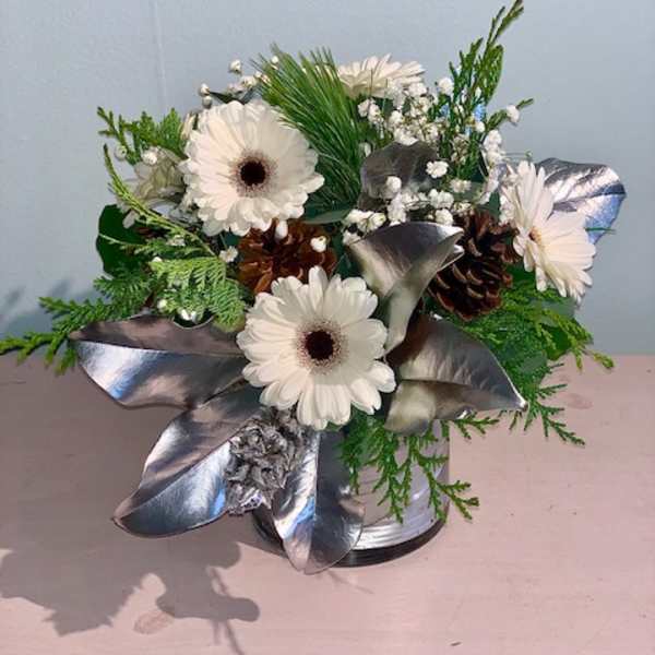 White gerbera daisies in a silver vase with pinecones and metallic leaves
