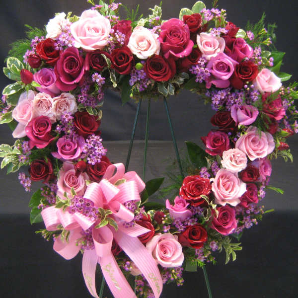 Heart-shaped rose wreath with pink ribbon bow on a stand