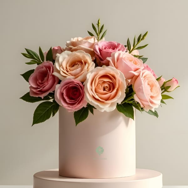 Pink and peach roses arranged in a round blush box