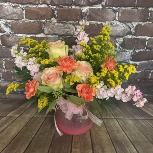 Pink and peach roses with yellow filler flowers in a round vase