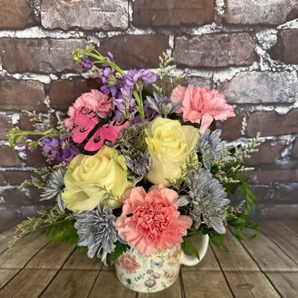 Bouquet of pastel flowers in a floral mug with a butterfly accent
