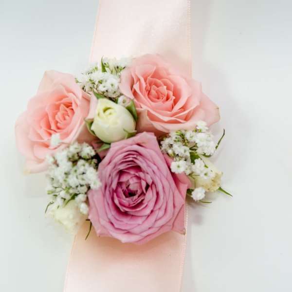Pink rose wrist corsage with white filler flowers on a pale ribbon