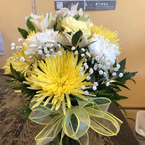 Yellow and white chrysanthemum bouquet in a glass vase with a ribbon