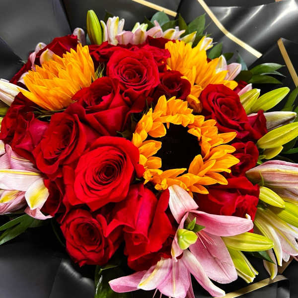 Bouquet of red roses, yellow sunflowers, and pink lilies wrapped in black paper
