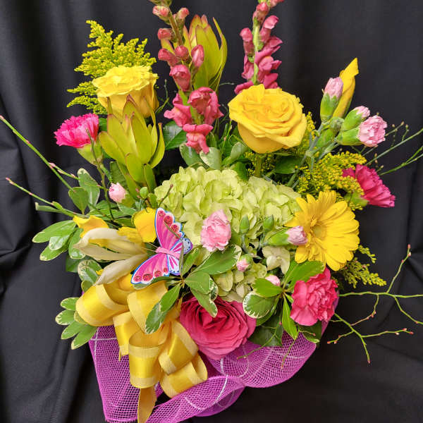 Bright mixed bouquet with yellow roses, pink blooms, and a purple ribbon wrap
