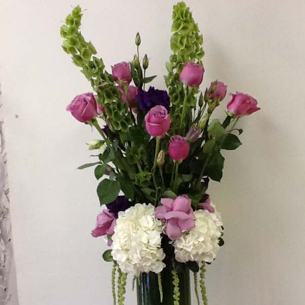 Tall bouquet of pink roses, white hydrangeas, and green hanging accents in a glass vase
