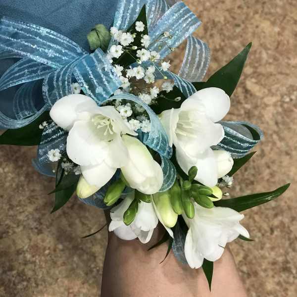 White floral wrist corsage with blue ribbon and baby's breath