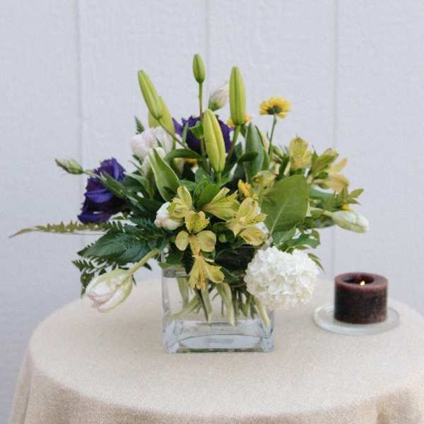 Mixed bouquet in a square glass vase beside a lit candle