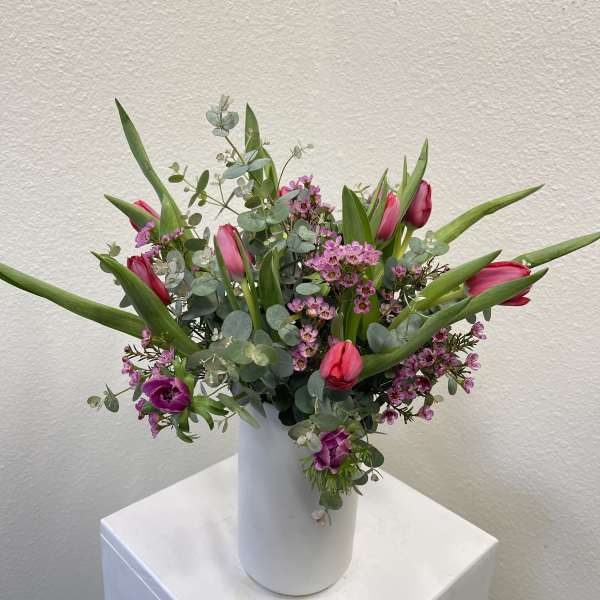 Tall white vase with pink tulips and small purple flowers in a loose, airy arrangement