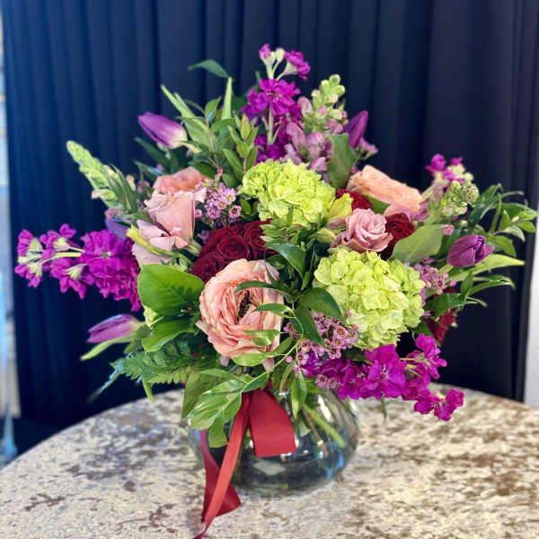Mixed pink and purple bouquet in a glass vase with a red ribbon
