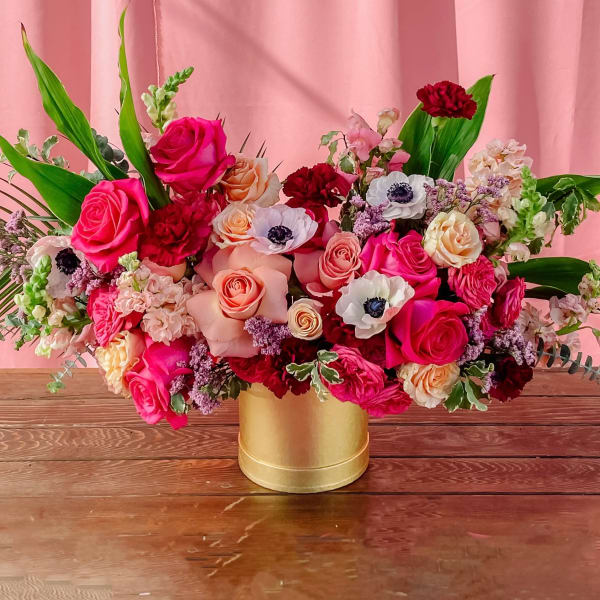 Mixed pink and red floral arrangement in a gold vase