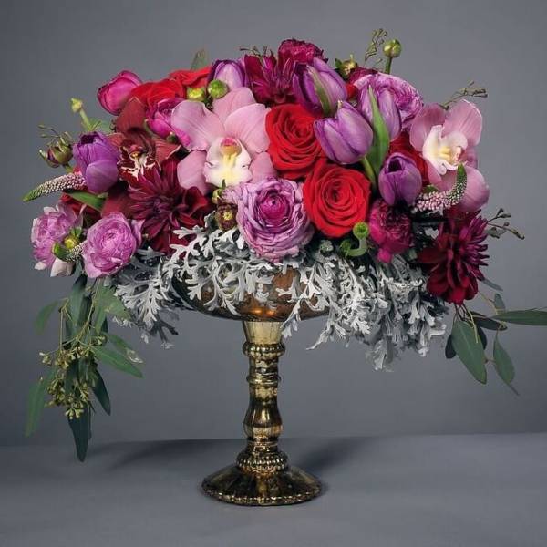 Mixed pink and red floral arrangement in a gold pedestal vase