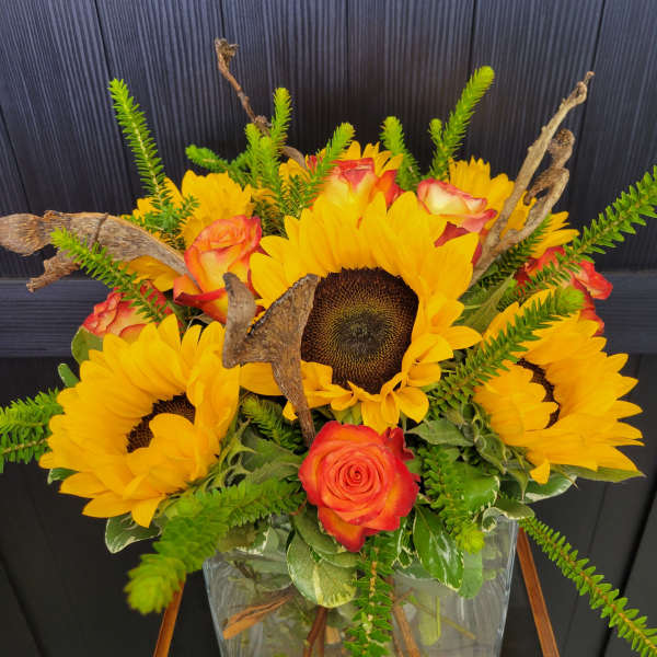 Sunflowers and orange roses arranged in a clear square vase