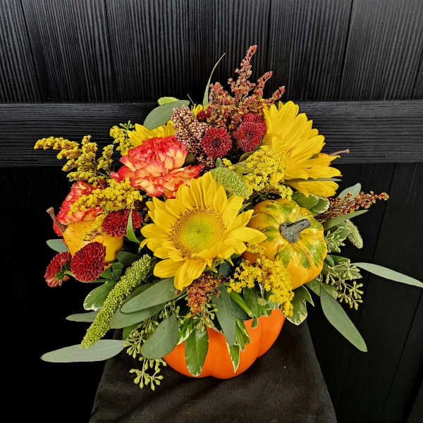 Fall floral arrangement in a pumpkin container with sunflowers and mums